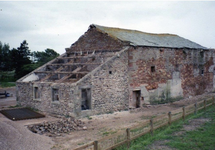 Stone barn during restoration, with exposed roof timbers, open doorways and a pile of reclaimed stone
