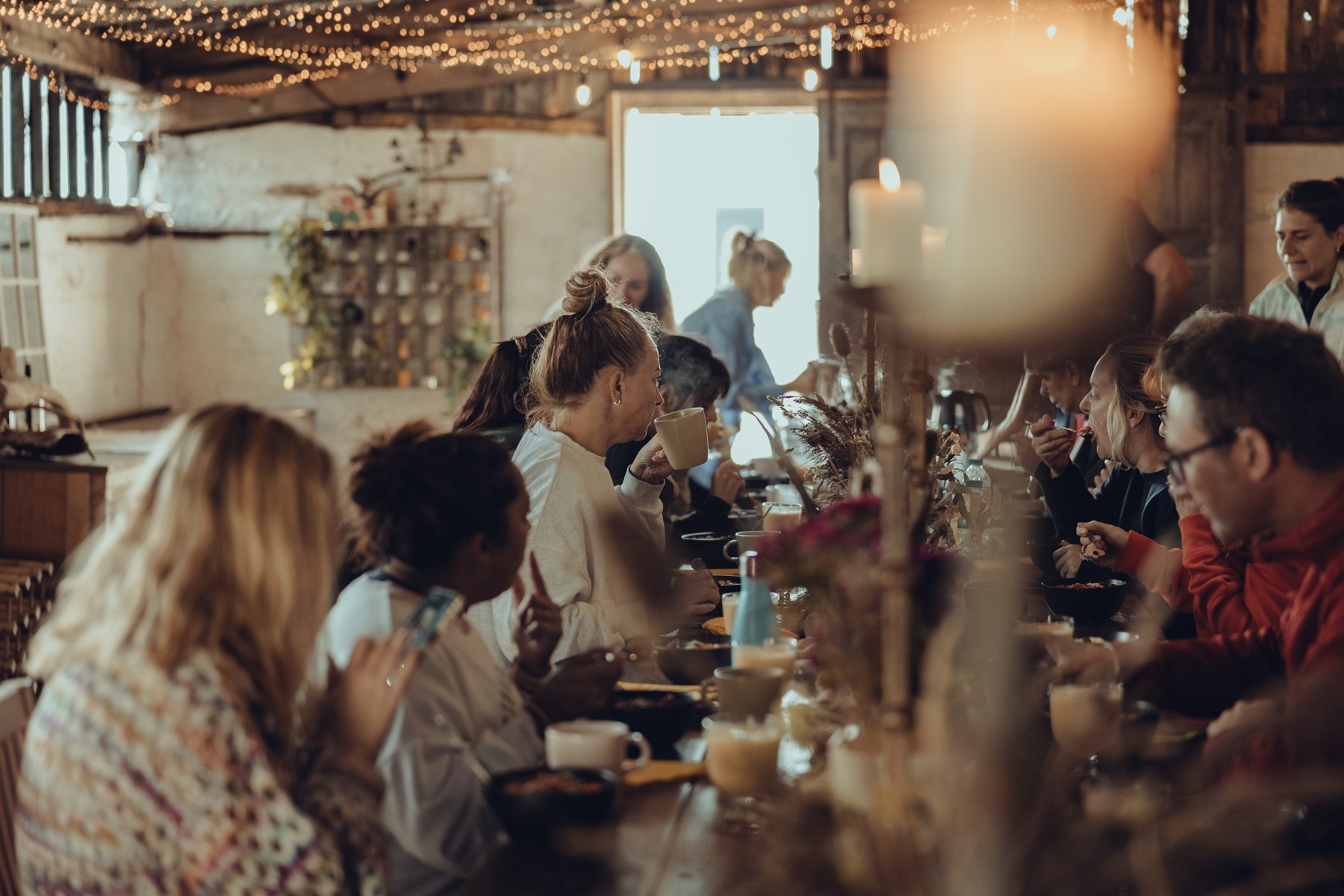 Guests sharing a meal around a long table beneath warm lights in The Out Barn at Patty’s Barn