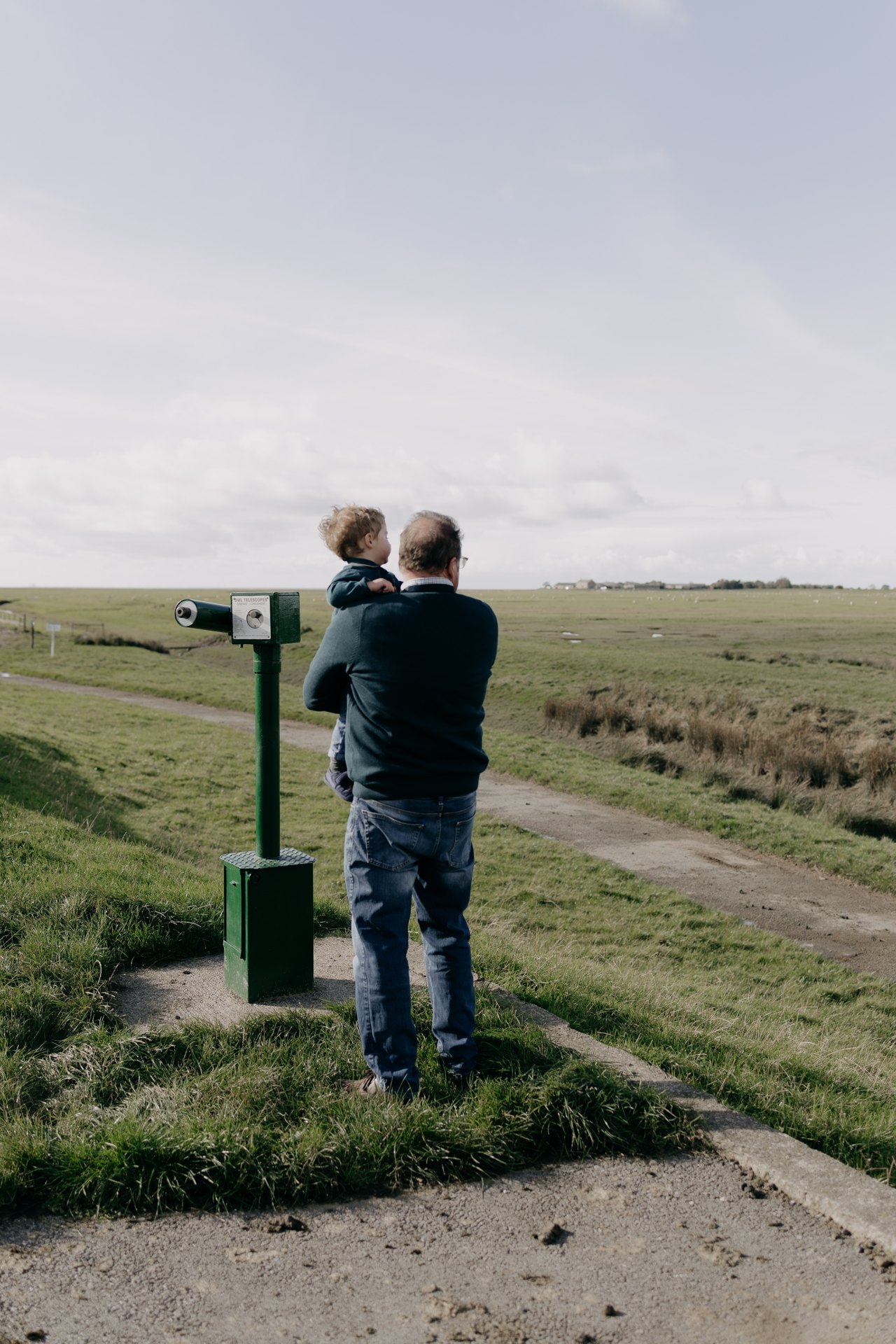 An adult and child looking across the coastal landscape beside a telescope
