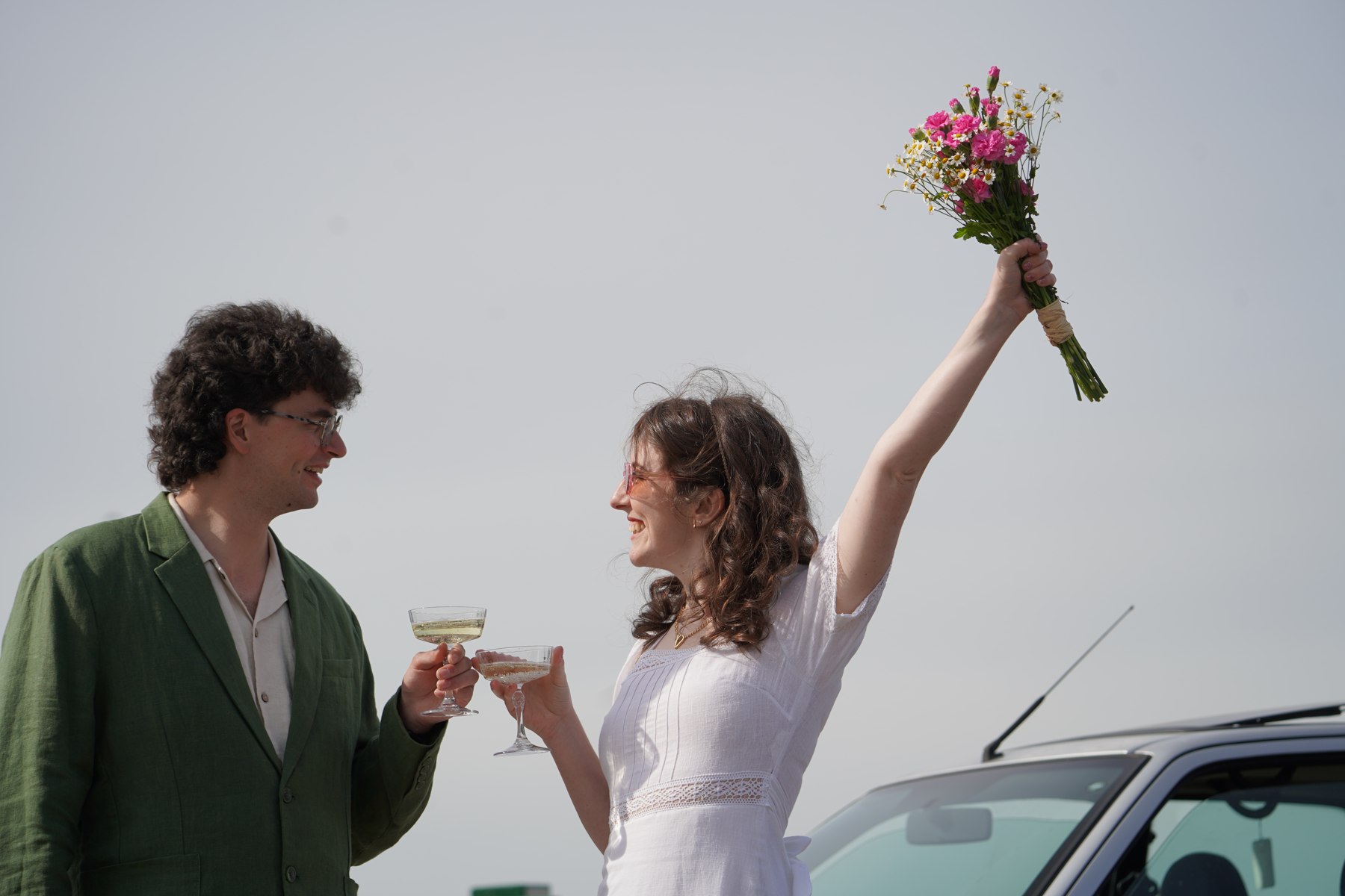 A wedding couple celebrating outdoors, raising glasses and a bouquet